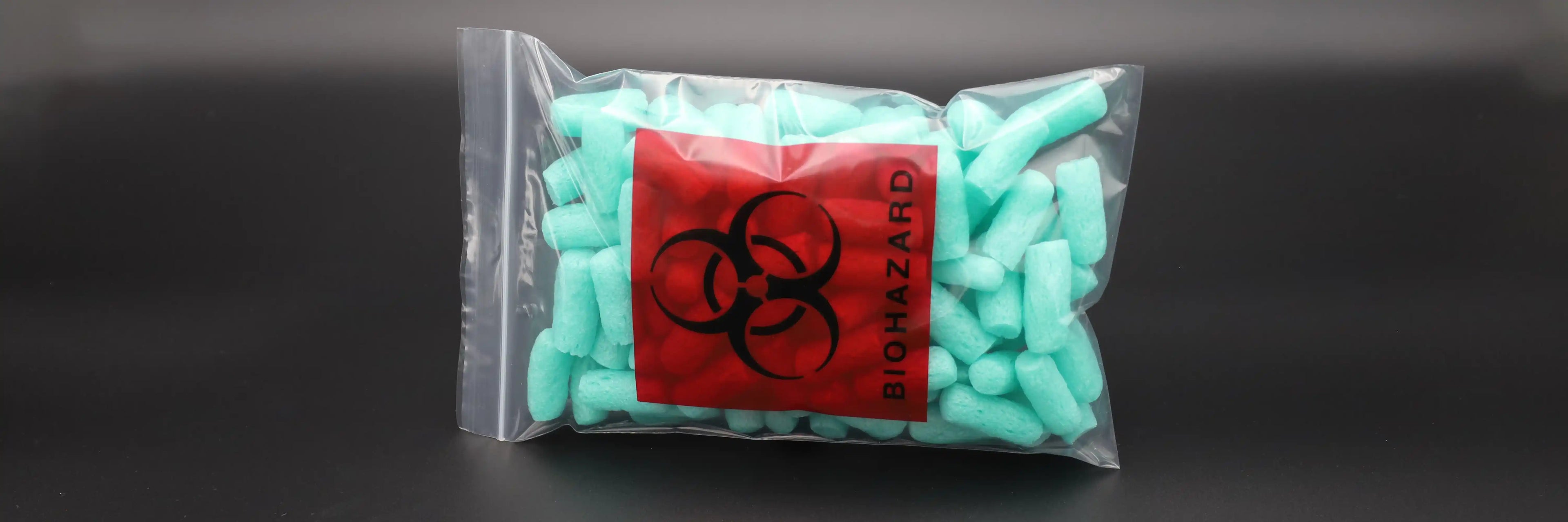 Transparenter Biohazard-Druckverschlussbeutel mit rotem Warnetikett – gefüllt mit türkisfarbenem Füllmaterial, ideal für medizinische Abfälle, Laborproben und kontaminierte Materialien.