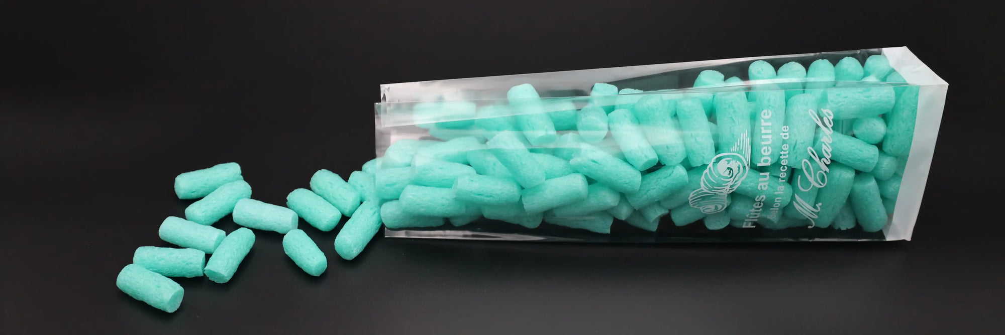 Transparenter Blockbodenbeutel mit weißem Aufdruck und türkisfarbenem Füllmaterial – stabile Lebensmittelverpackung mit hoher Standfestigkeit, ideal für Süßwaren, Gebäck oder Feinkostartikel im Einzelhandel.