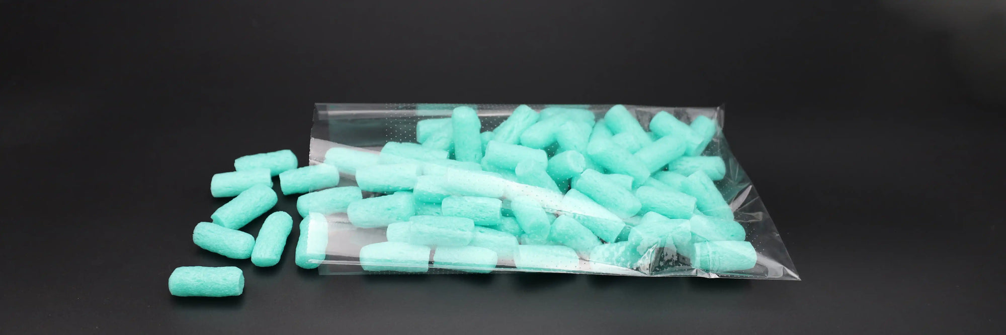 „Transparenter, mikroperforierter Kunststoffbeutel – liegend auf schwarzer Fläche, befüllt mit türkisfarbenem Verpackungsmaterial, teilweise geöffnet mit herausgefallenem Inhalt.“